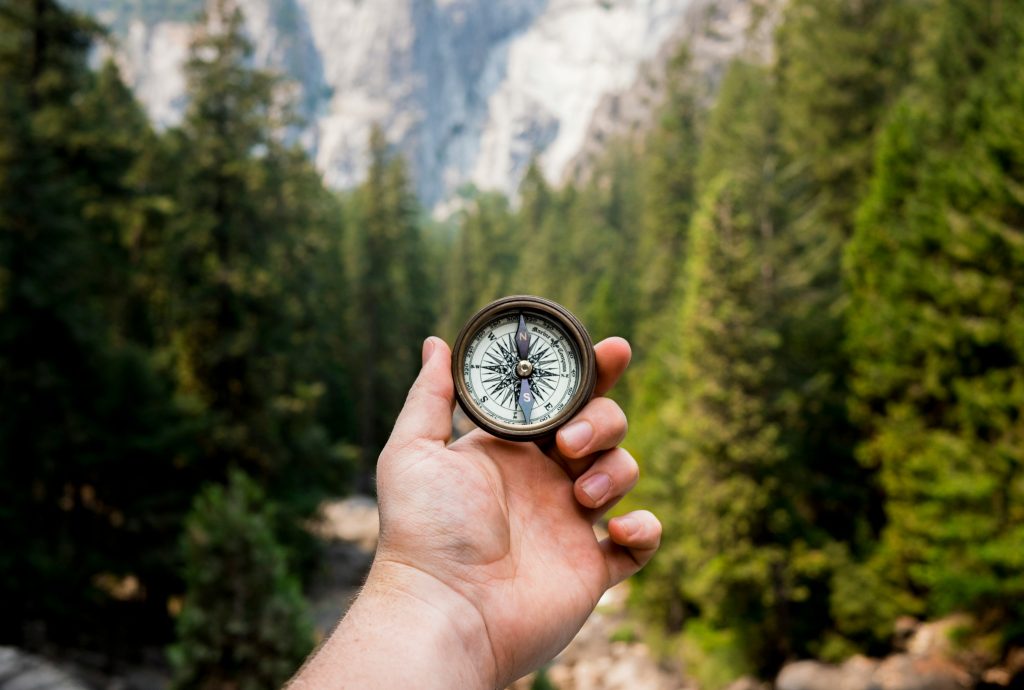 compass forest image A hand holds up a compass in the middle of the woods
